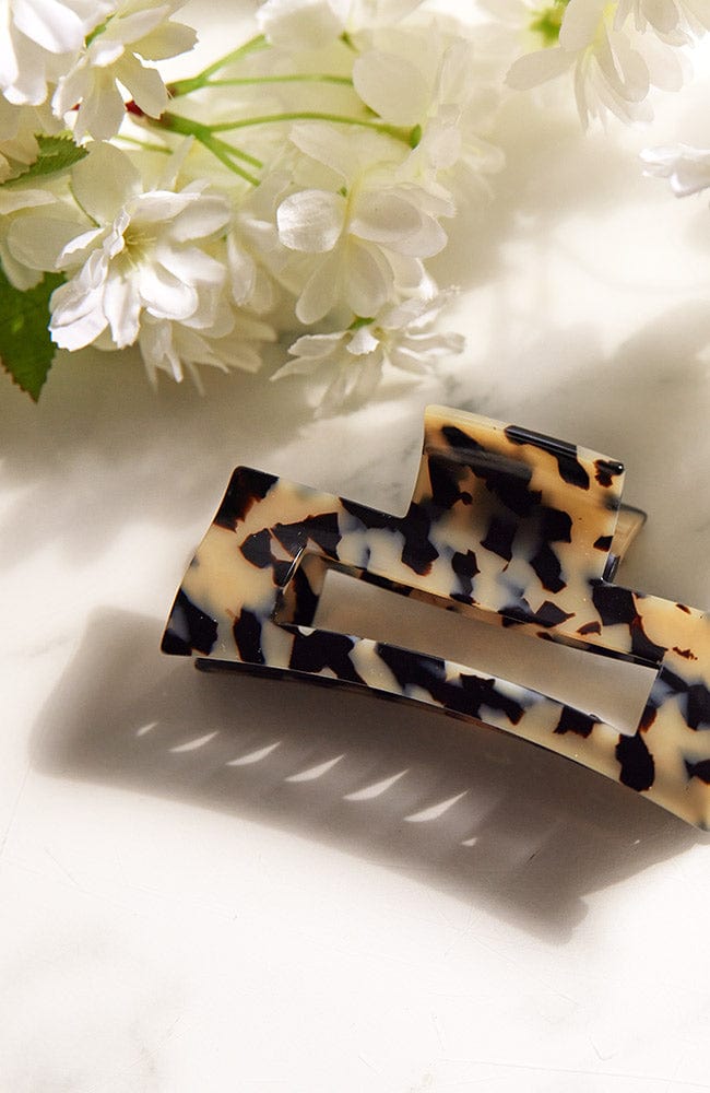 flowers next to a large hair clip with an elegant cutout design and sophisticated ivory and black coloring